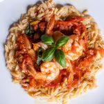 top down view of plated tomato poached shrimp with orzo and red sauce
